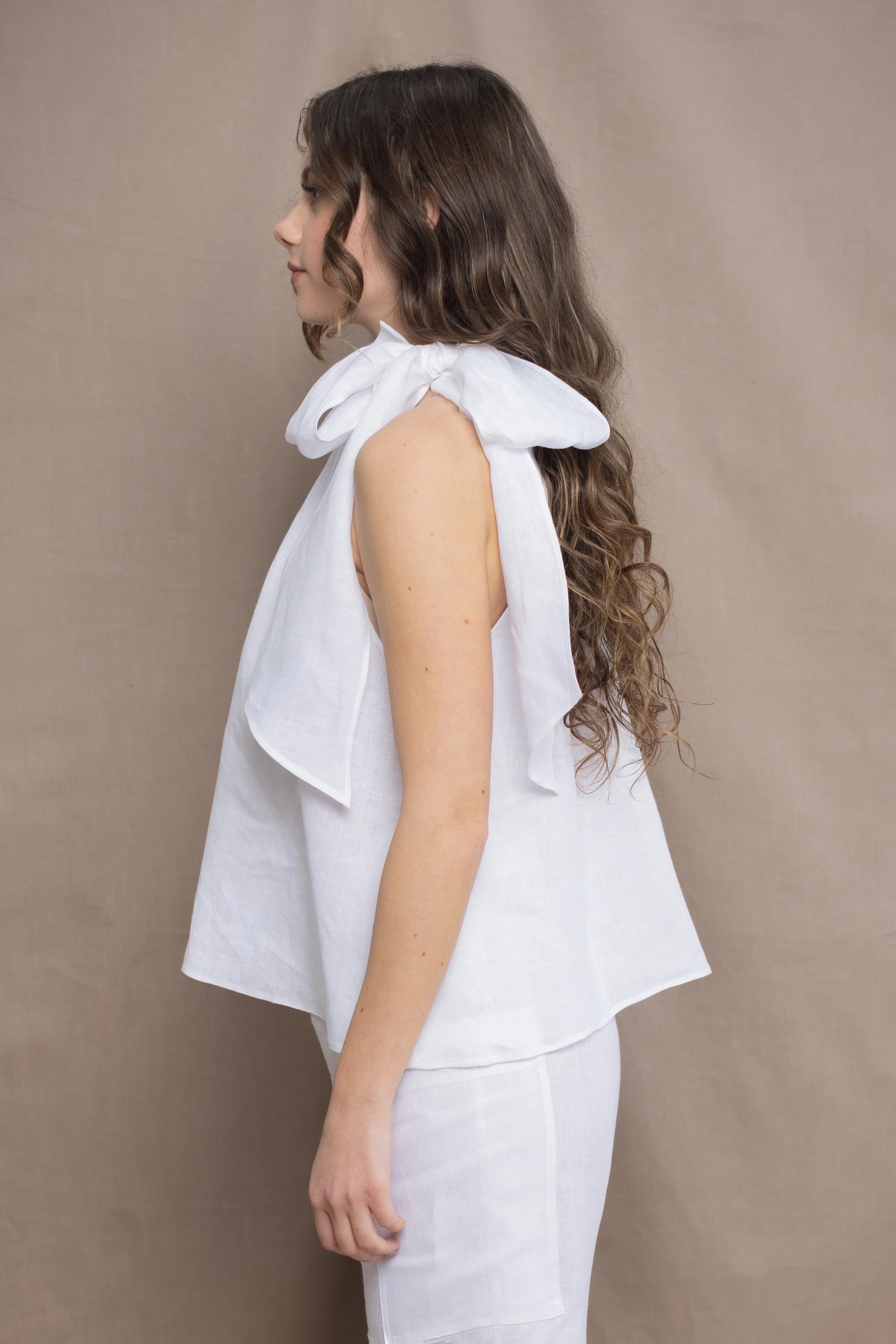 a woman wears an Irish linen halter top with bow detailing on the shoulder in white with matching white linen trousers 