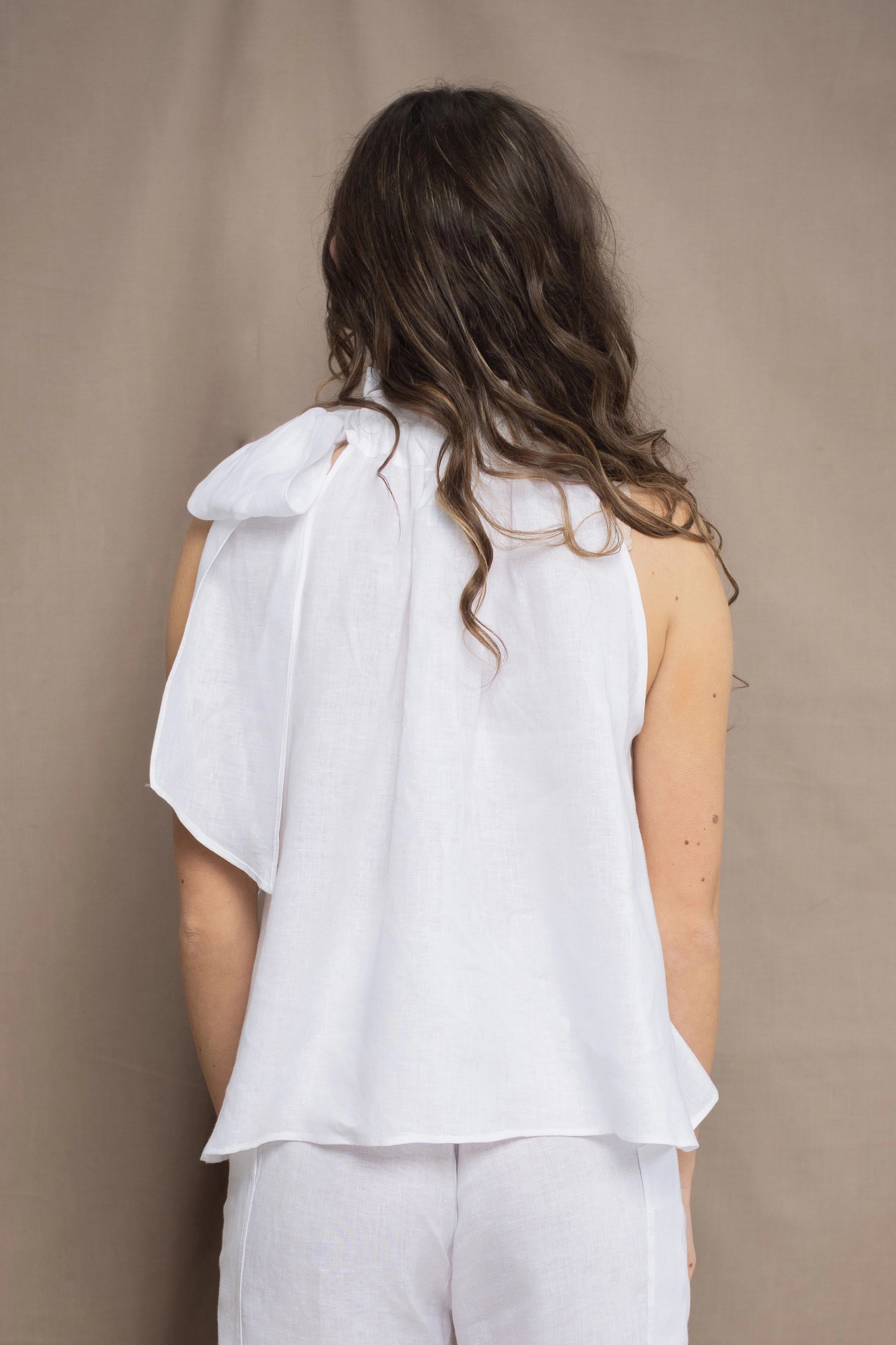 a woman wears an Irish linen halter top with bow detailing on the shoulder in white with matching white linen trousers 