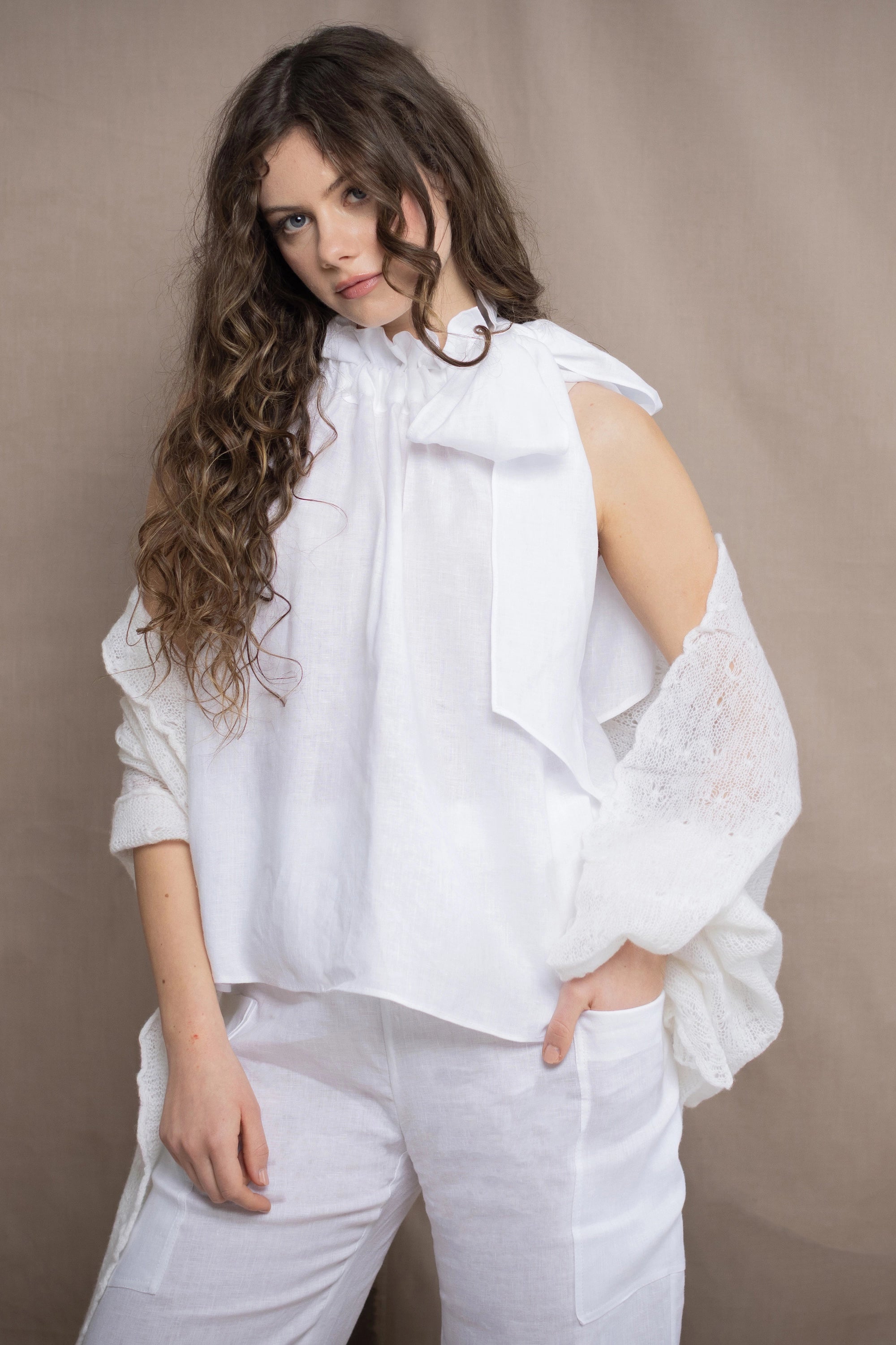 a woman wears an Irish linen halter top with bow detailing on the shoulder in white with matching white linen trousers and white cashmere wrap shawl in white