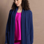A woman wears an open style longer cashmere cardigan in blue worn over a bright pink 100% silk top and matching skirt