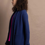A woman wears an open style longer cashmere cardigan in blue worn over a bright pink 100% silk top and matching skirt