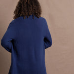 A woman wears an open style longer cashmere cardigan in blue worn over a bright pink 100% silk top and matching skirt