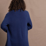 A woman wears an open style longer cashmere cardigan in blue worn over a bright pink 100% silk top and matching skirt