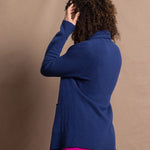 A woman wears an open style longer cashmere cardigan in blue worn over a bright pink 100% silk top and matching skirt