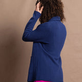 A woman wears an open style longer cashmere cardigan in blue worn over a bright pink 100% silk top and matching skirt