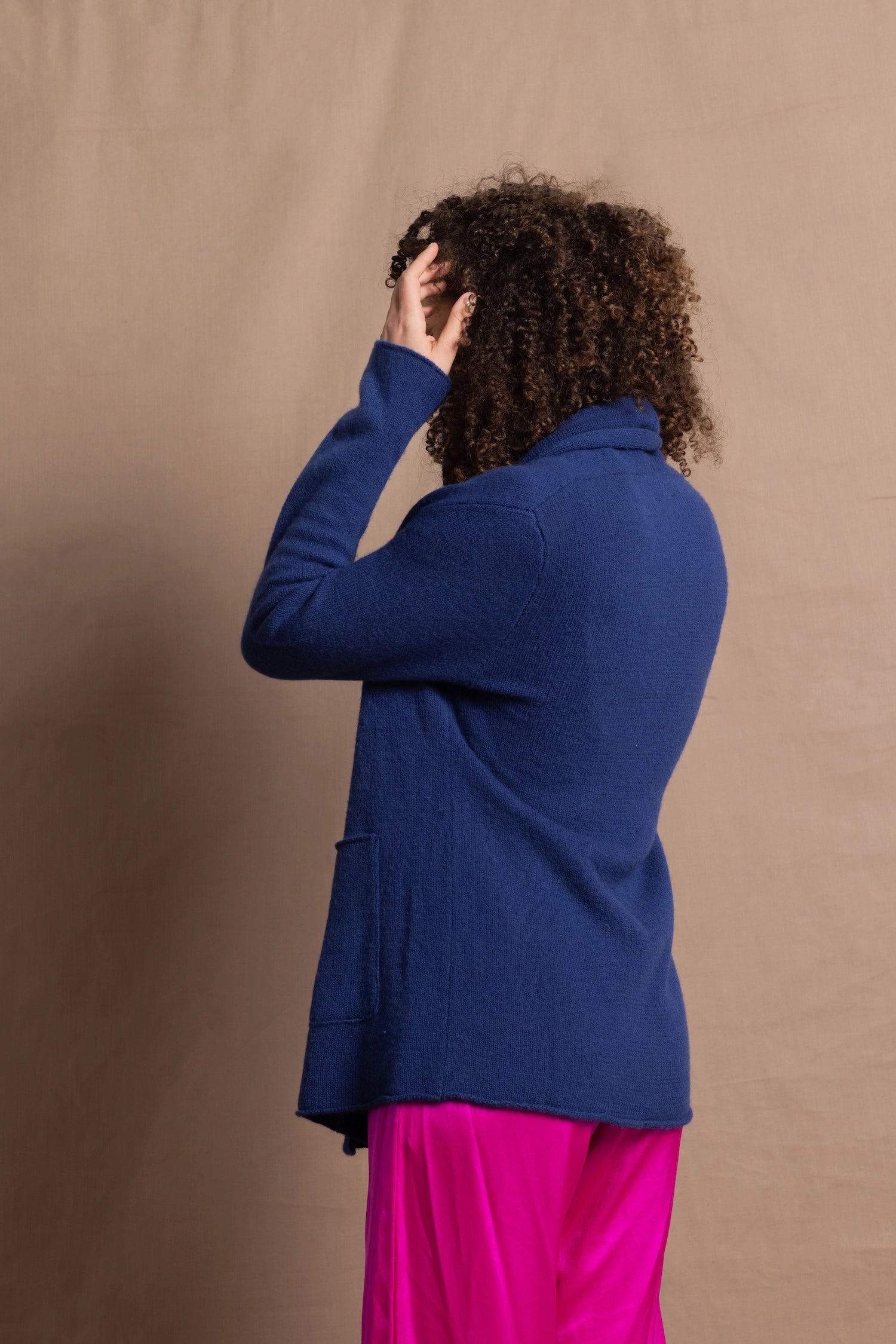A woman wears an open style longer cashmere cardigan in blue worn over a bright pink 100% silk top and matching skirt
