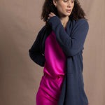 A woman wears a long cashmere cardigan in inky blue colour over bright pink silk top and skirt