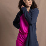 A woman wears a long cashmere cardigan in inky blue colour over bright pink silk top and skirt