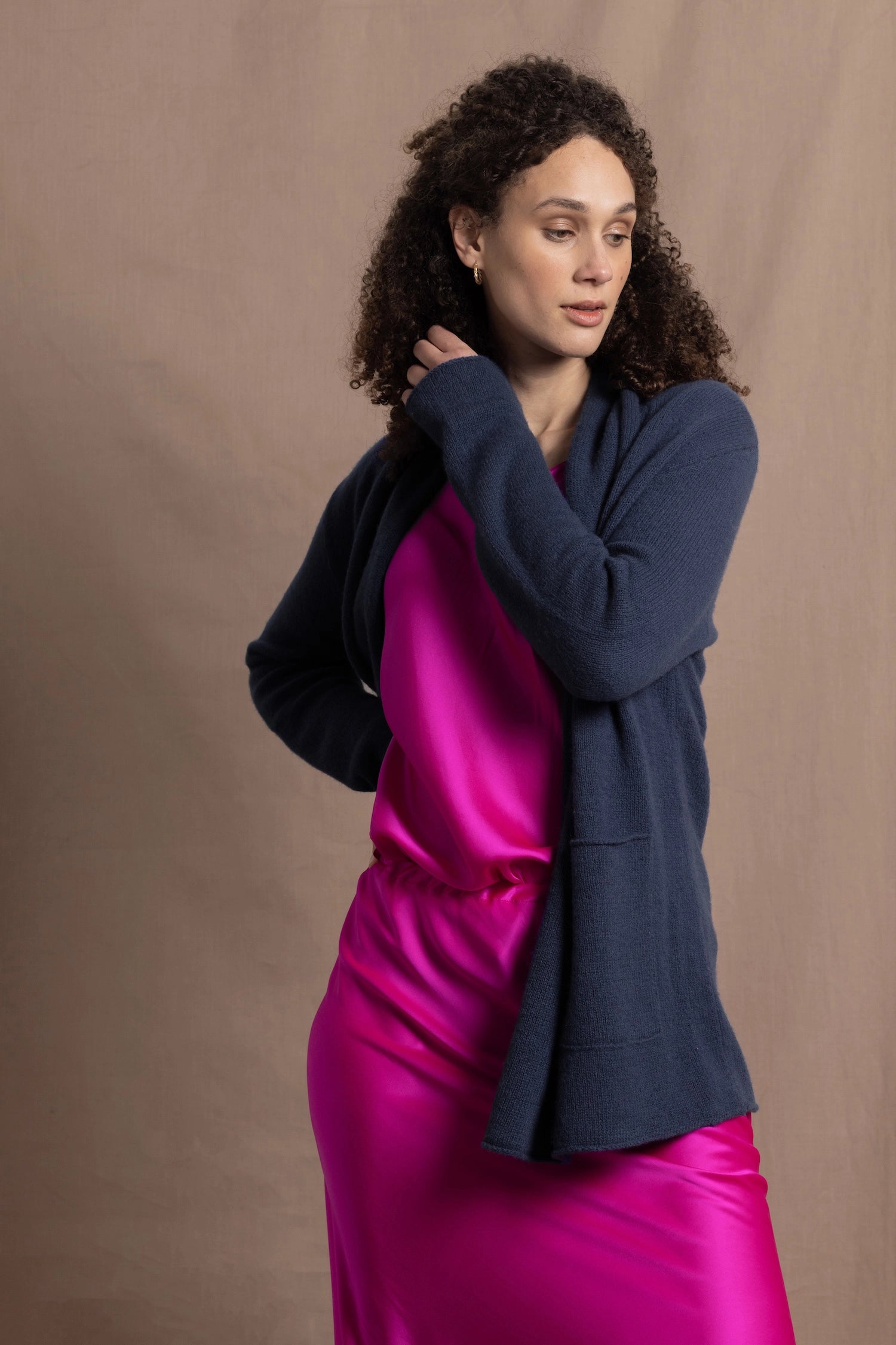 A woman wears a long cashmere cardigan in inky blue colour over bright pink silk top and skirt