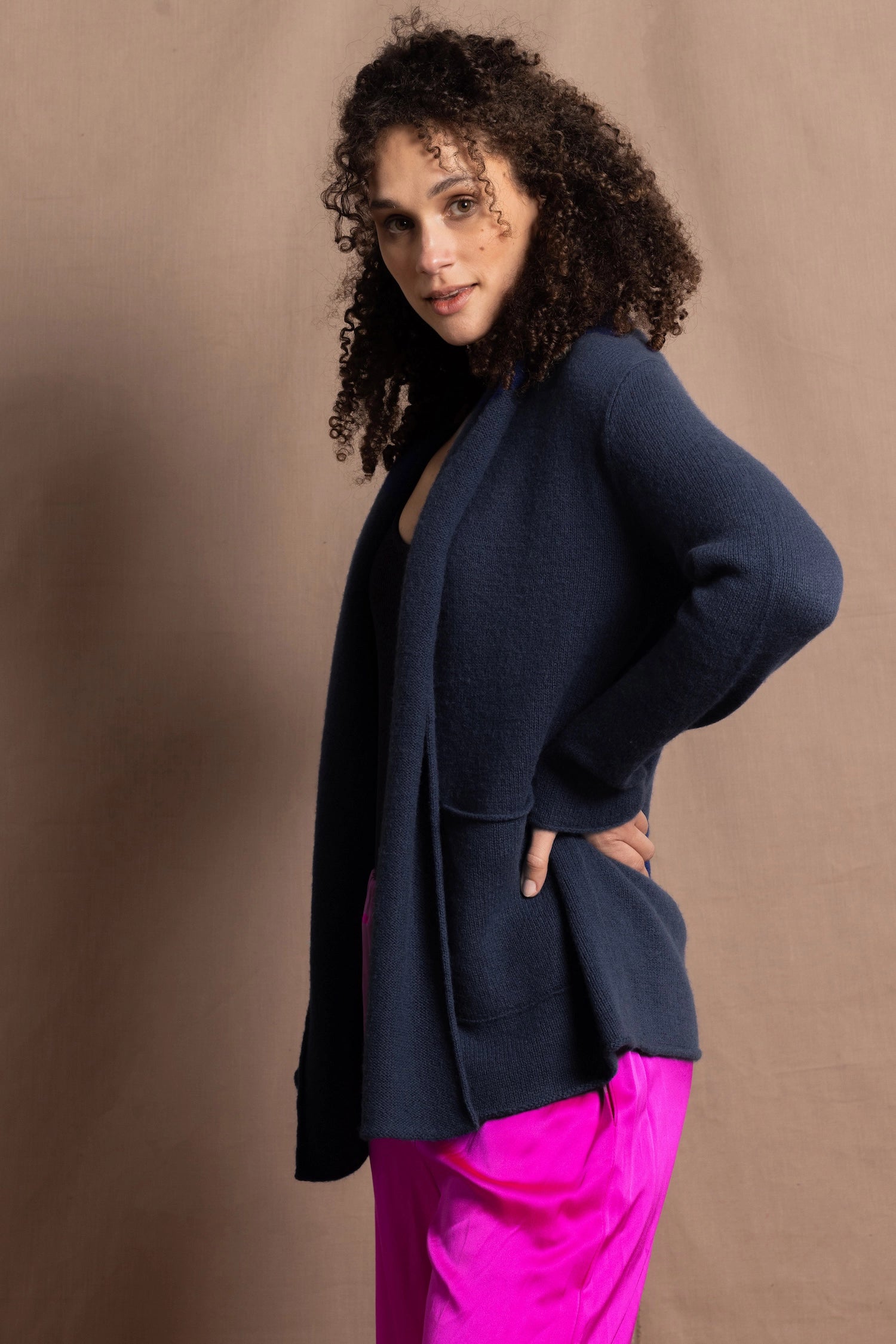A woman wears a long cashmere cardigan in inky blue colour over bright pink silk trousers