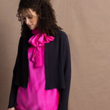 A woman wears a 100% silk pussy bow top in bright pink with matching trousers and a navy cropped cashmere cardigan on top