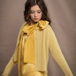 a woman wears a pure 100% cashmere cropped cardigan sweater in butter yellow over silk clothing in butter yellow