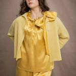 a woman wears a pure 100% cashmere cropped cardigan sweater in butter yellow over silk clothing in butter yellow
