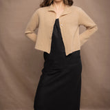 a woman wears a cropped cashmere cardigan in a sandy beige colour over black linen top and skirt by Irish brand Madigan