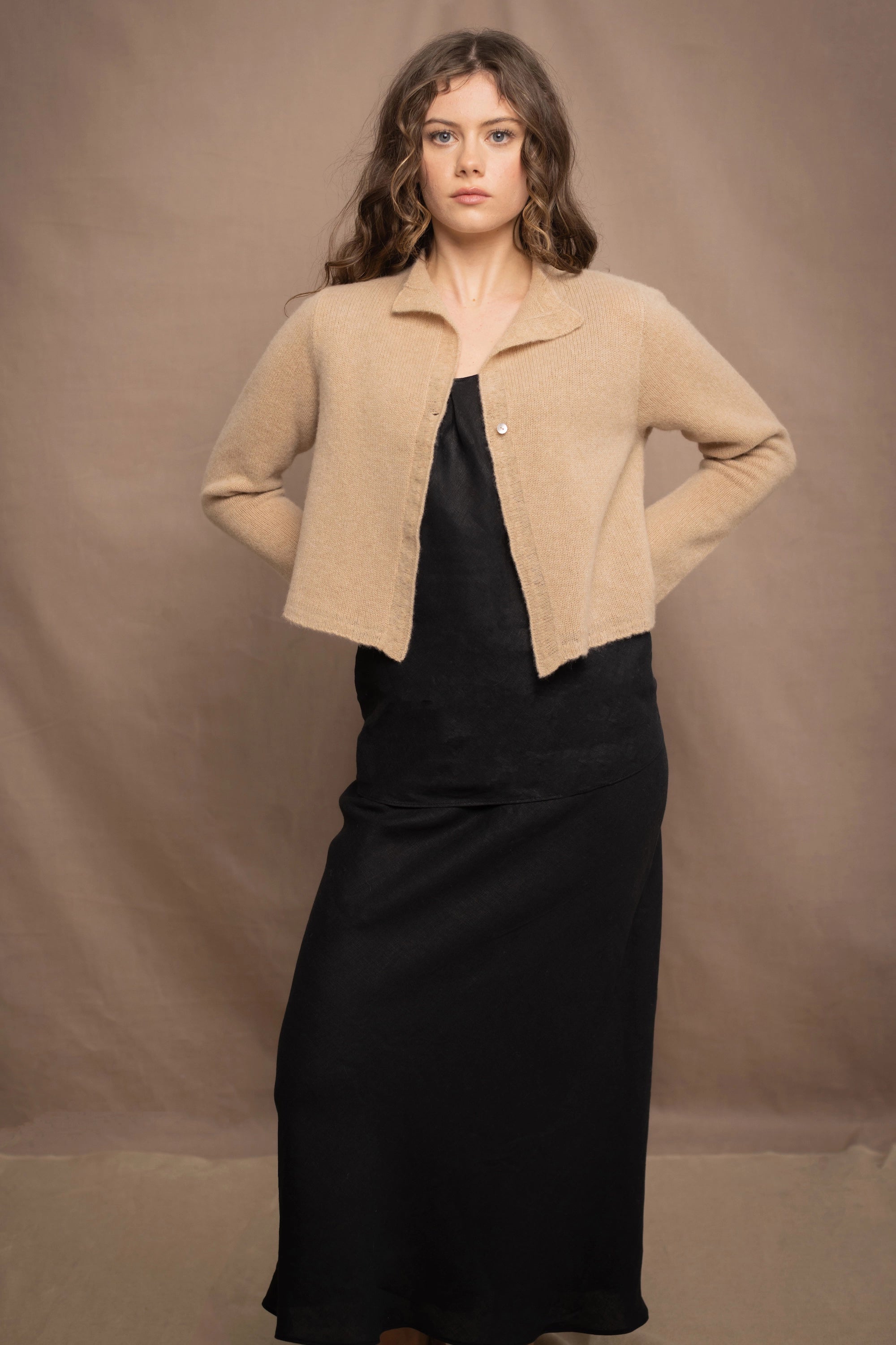 a woman wears a cropped cashmere cardigan in a sandy beige colour over black linen top and skirt by Irish brand Madigan