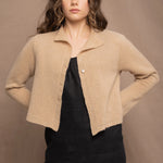 a woman wears a cropped cashmere cardigan in a sandy beige colour over black linen top and skirt by Irish brand Madigan