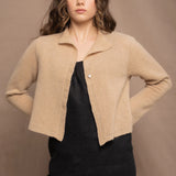 a woman wears a cropped cashmere cardigan in a sandy beige colour over black linen top and skirt by Irish brand Madigan