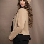 a woman wears a cropped cashmere cardigan in a sandy beige colour with matching beanie hat over black linen top and skirt by Irish brand Madigan