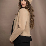 a woman wears a cropped cashmere cardigan in a sandy beige colour with matching beanie hat over black linen top and skirt by Irish brand Madigan