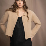 a woman wears a cropped cashmere cardigan in a sandy beige colour with matching beanie hat over black linen top and skirt by Irish brand Madigan