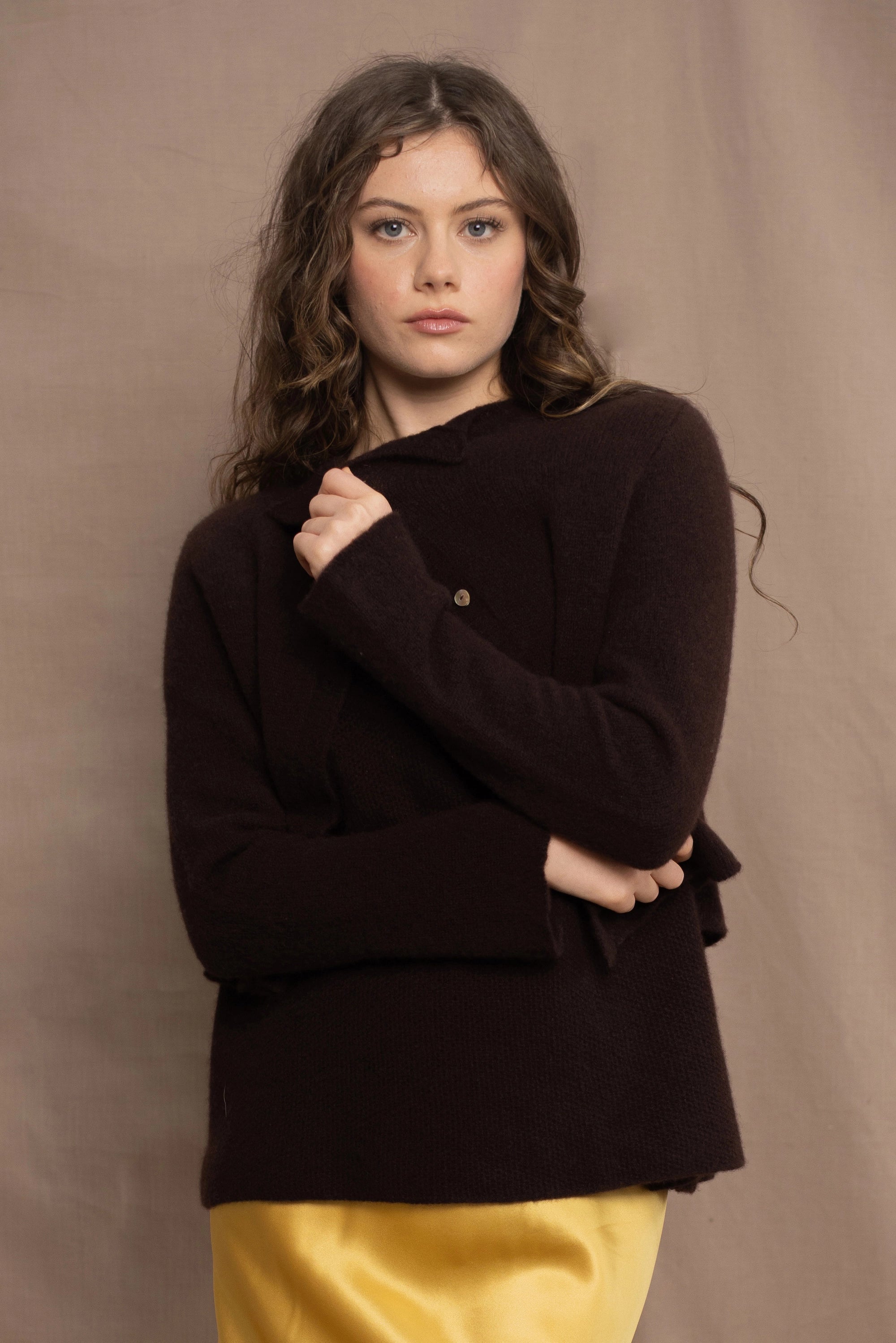 a woman wears a cropped cashmere cardigan in chocolate brown over a matching cashmere tee sweater with a silk skirt in pale yellow