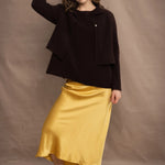 a woman wears a cropped cashmere cardigan in chocolate brown over a matching cashmere tee sweater with a silk skirt in pale yellow