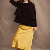 a woman wears a cropped cashmere cardigan in chocolate brown over a matching cashmere tee sweater with a silk skirt in pale yellow