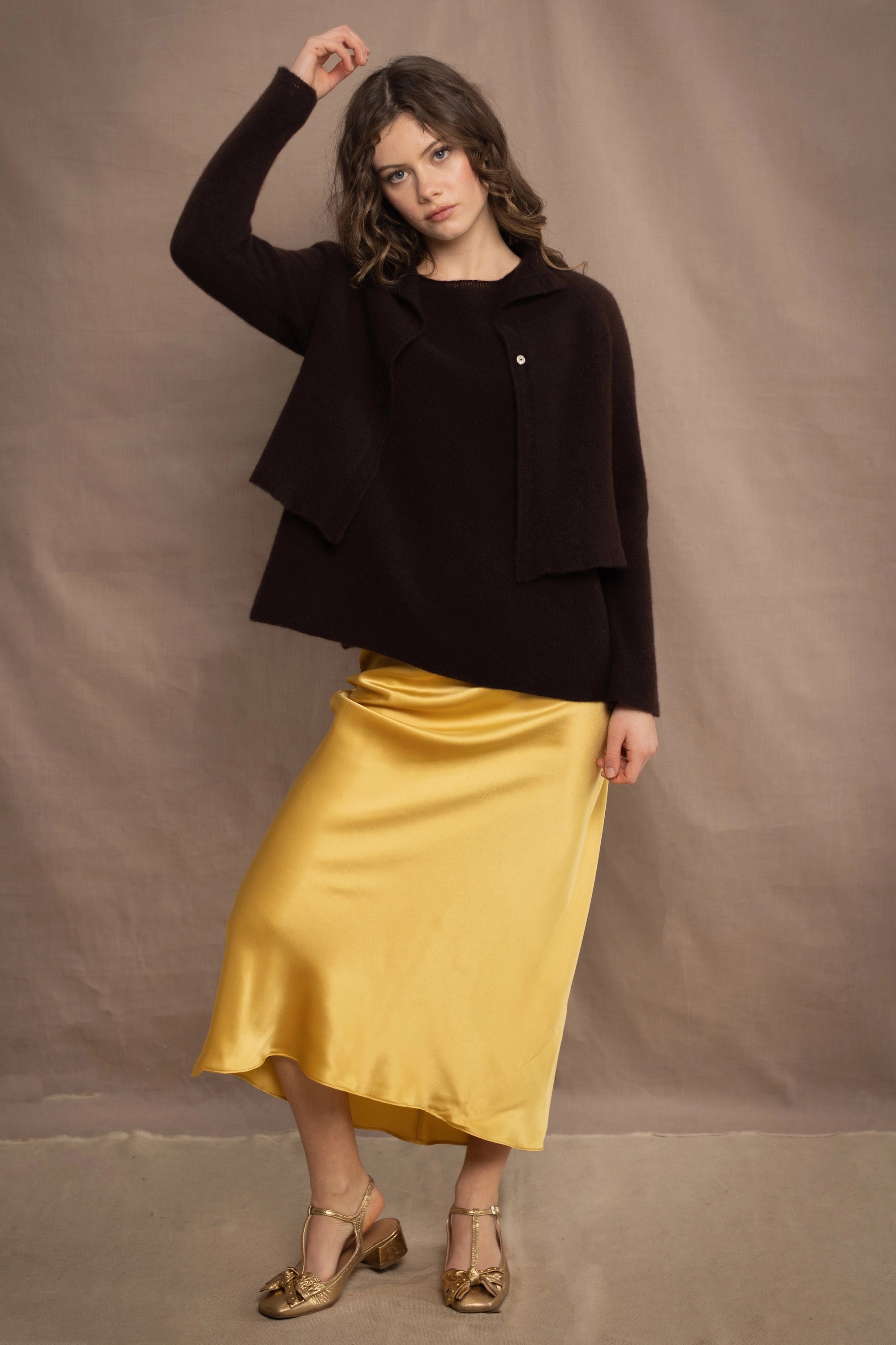 a woman wears a cropped cashmere cardigan in chocolate brown over a matching cashmere tee sweater with a silk skirt in pale yellow