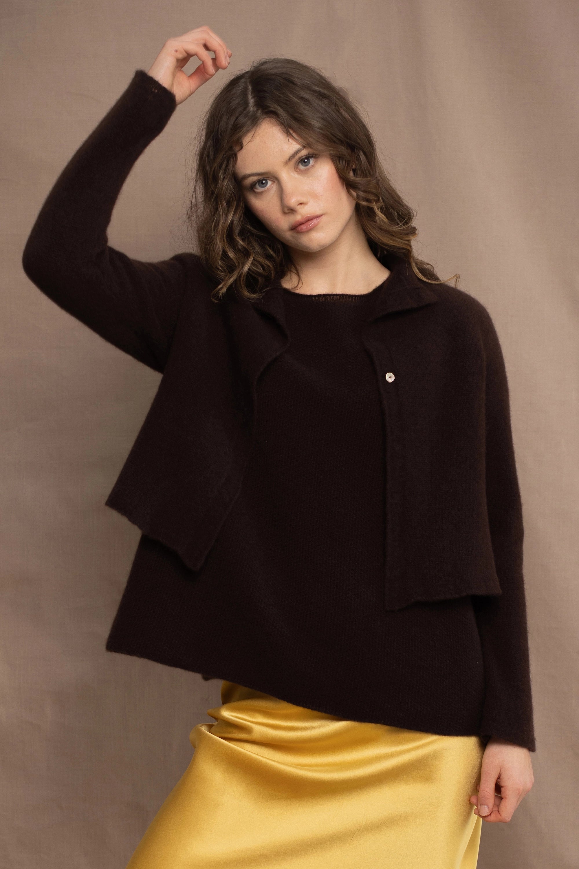 a woman wears a cropped cashmere cardigan in chocolate brown over a matching cashmere tee sweater with a silk skirt in pale yellow