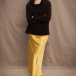 a woman wears a cropped cashmere cardigan in chocolate brown over a matching cashmere tee sweater with a silk skirt in pale yellow