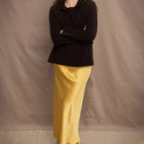 a woman wears a cropped cashmere cardigan in chocolate brown over a matching cashmere tee sweater with a silk skirt in pale yellow