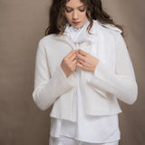 a woman wears an Irish linen halter top with bow detailing on the shoulder in white with matching white linen trousers with cropped cashmere cardigan over top in almost white