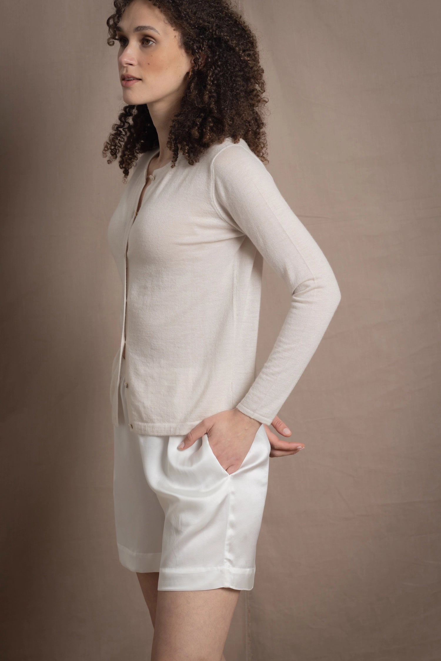 a woman wears a thin summer weight cashmere cardigan sweater in a cream colour with white silk shorts