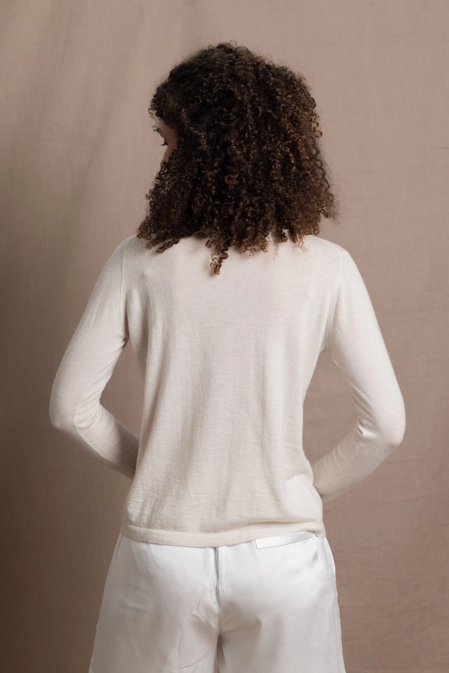 a woman wears a thin summer weight cashmere cardigan sweater in a cream colour with white silk shorts