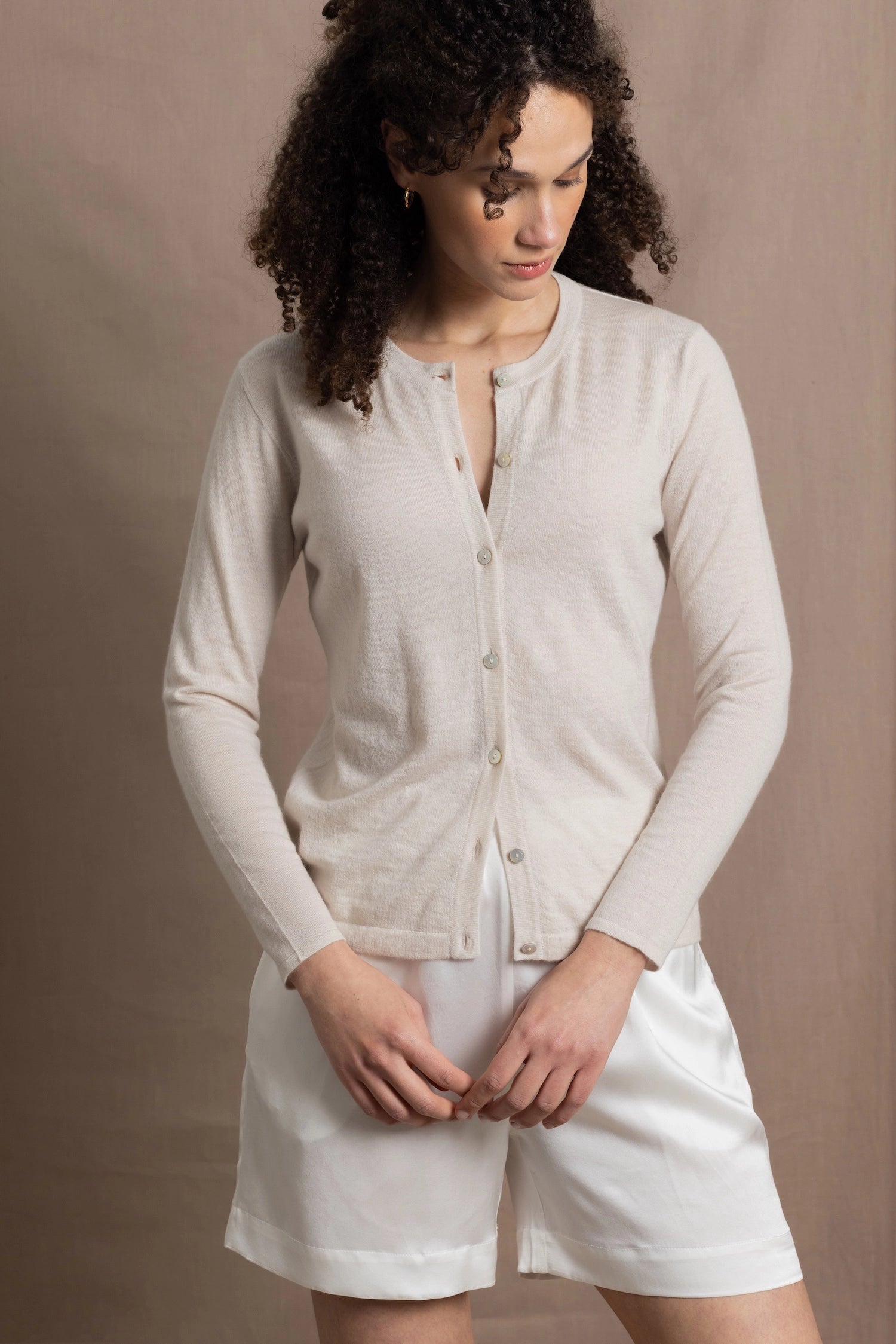 a woman wears a thin summer weight cashmere  button down cardigan sweater in a cream colour with white silk shorts