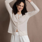 a woman wears a thin summer weight cashmere  button down cardigan sweater in a cream colour with white silk shorts