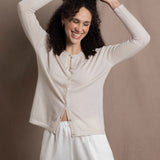 a woman wears a thin summer weight cashmere  button down cardigan sweater in a cream colour with white silk shorts