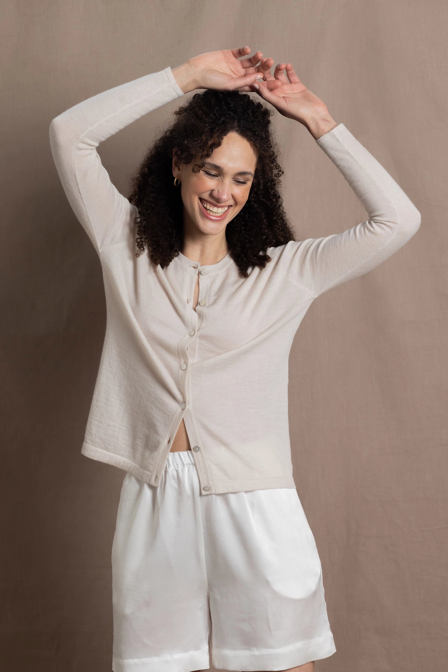 a woman wears a thin summer weight cashmere  button down cardigan sweater in a cream colour with white silk shorts