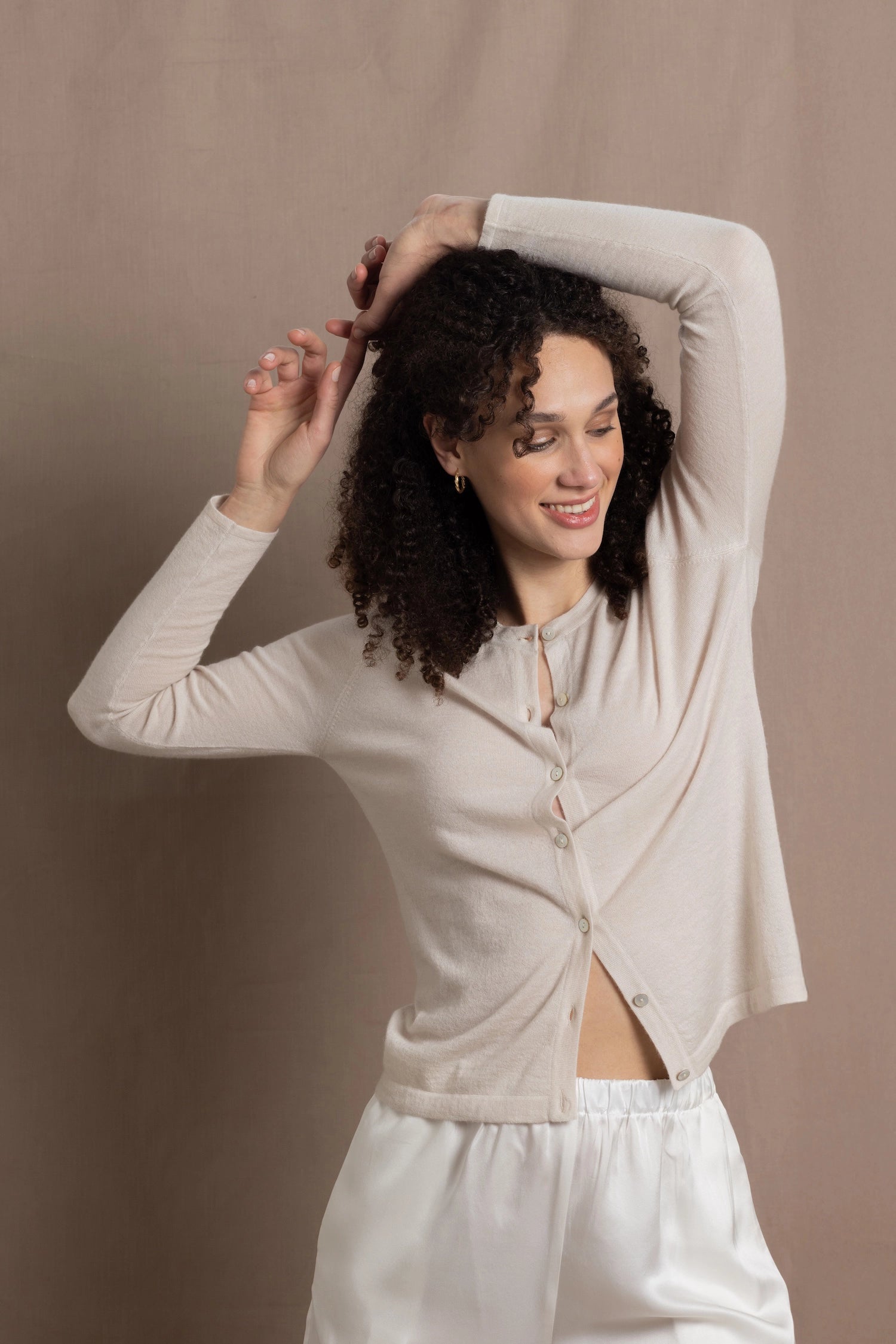a woman wears a thin summer weight cashmere  button down cardigan sweater in a cream colour with white silk shorts