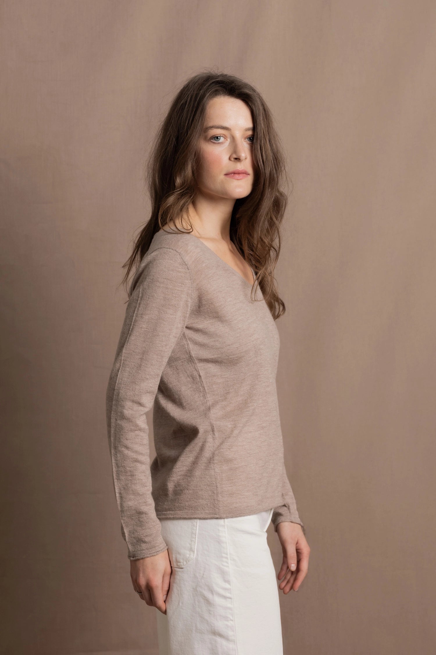 a woman wears a v neck thin summer weight cashmere sweater in a taupe colour and white jeans