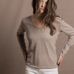 a woman wears a v neck thin summer weight cashmere sweater in a taupe colour and white jeans