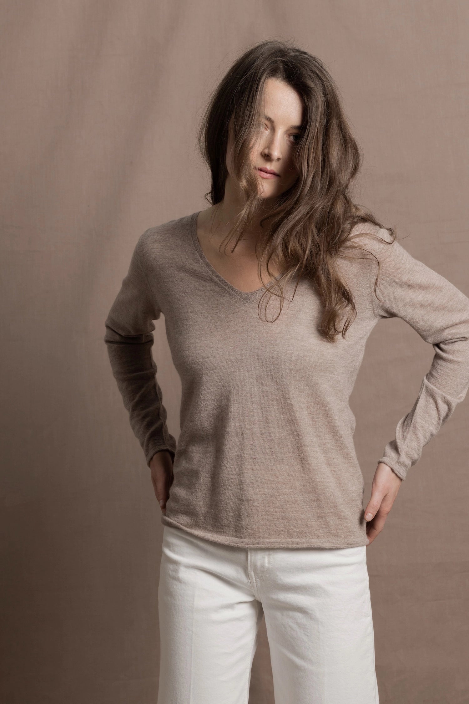 a woman wears a v neck thin summer weight cashmere sweater in a taupe colour and white jeans
