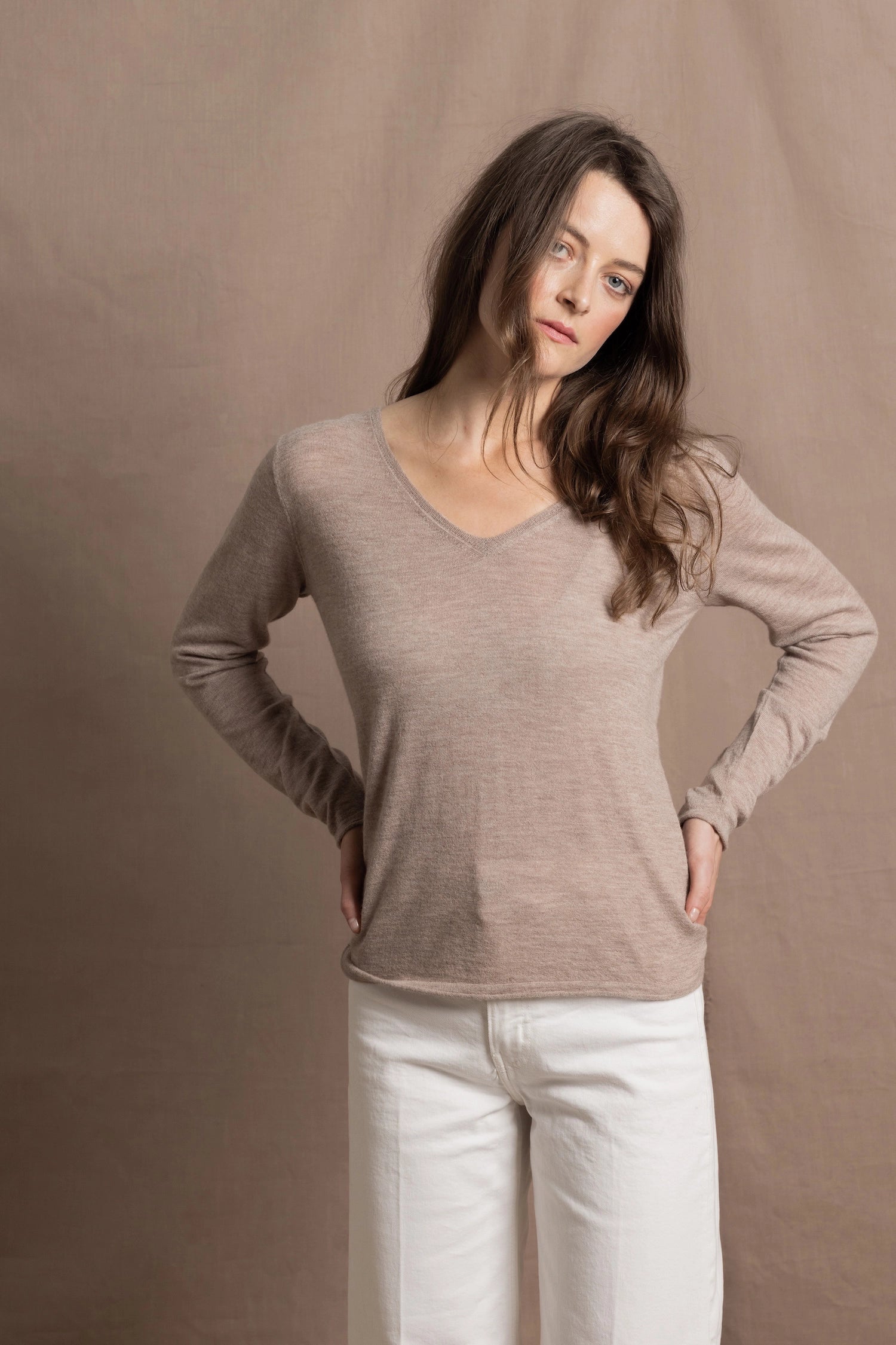 a woman wears a v neck thin summer weight cashmere sweater in a taupe colour and white jeans