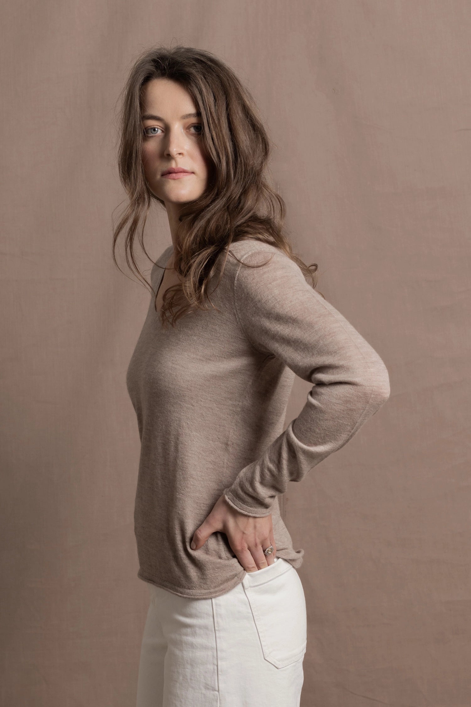 a woman wears a v neck thin summer weight cashmere sweater in a taupe colour and white jeans