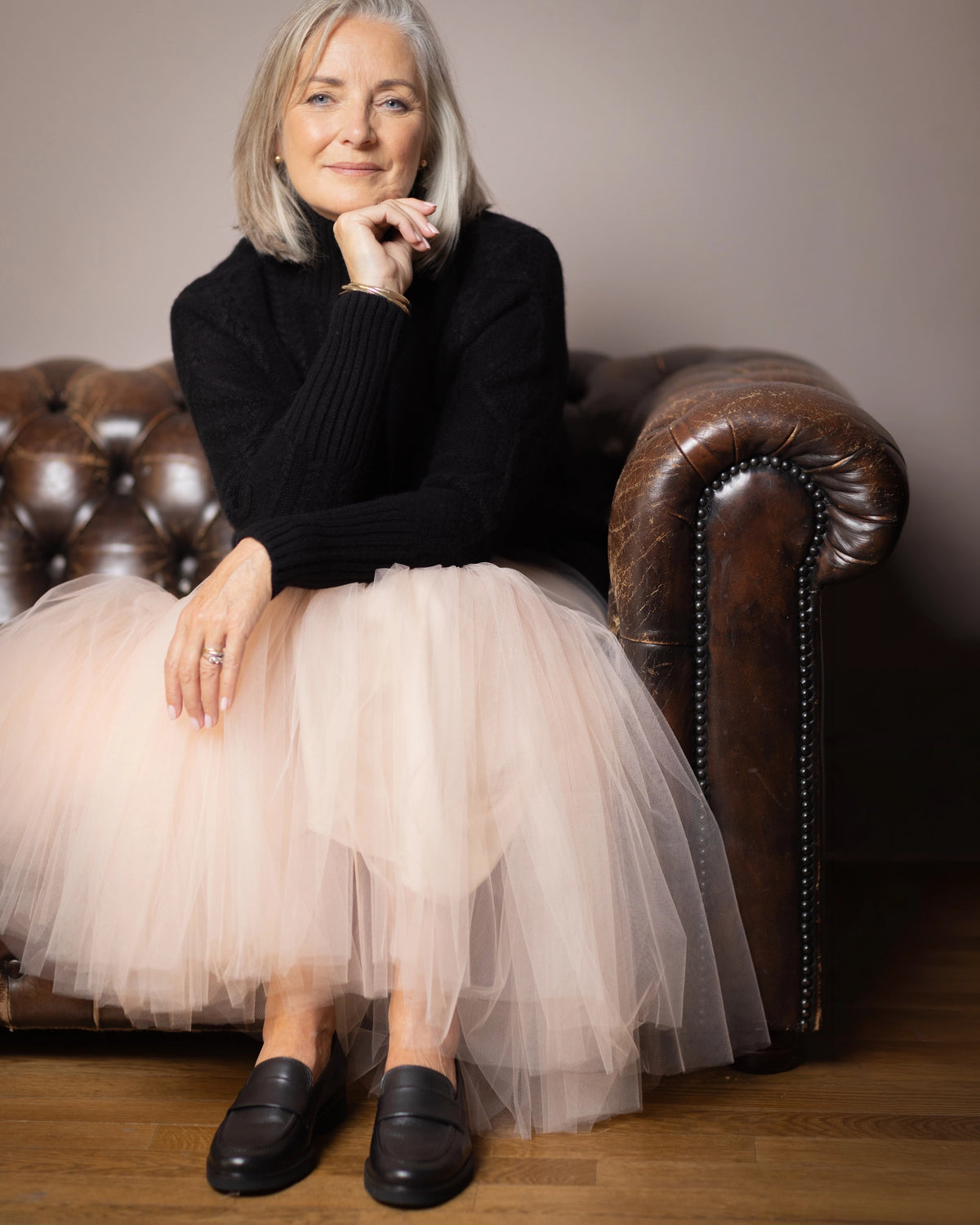 An older elegant woman wearing a luxurious black cashmere aran sweater jumper and a voluminous light pink tulle skirt by Irish brand Madigan