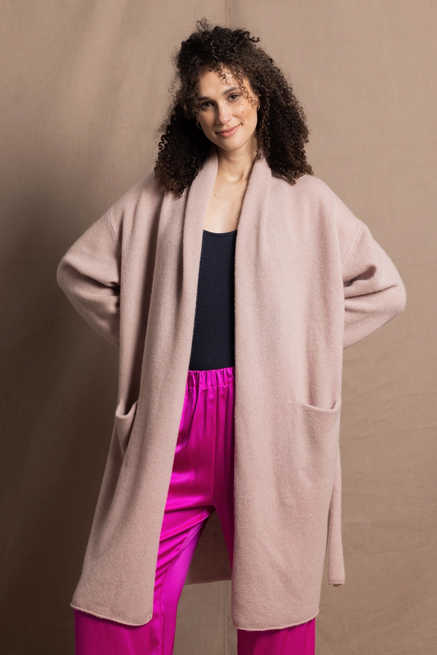 A woman wears a pure 100% cashmere dressing gown or robe in dusty pink with bright shocking pink silk trousers