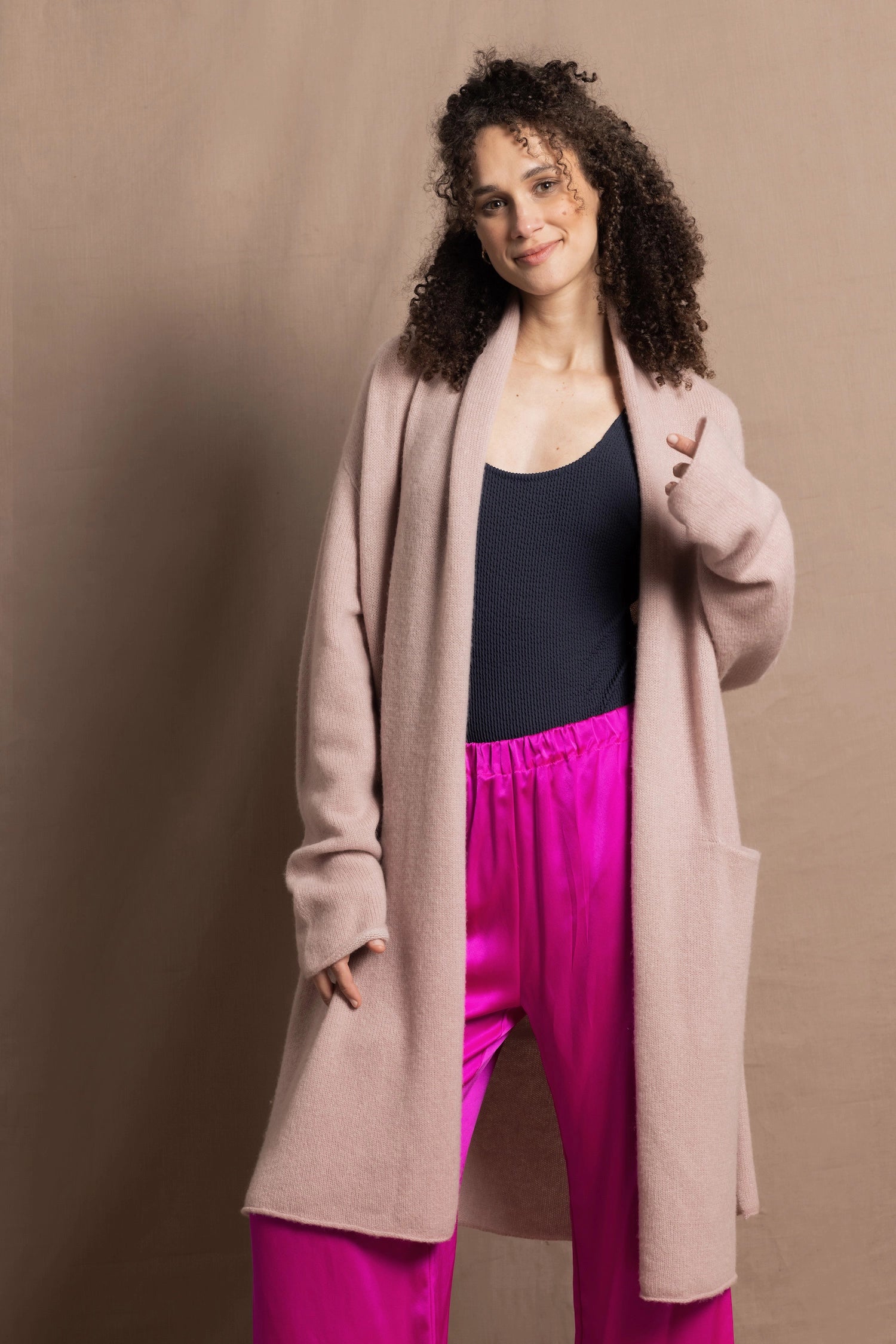 A woman wears a pure 100% cashmere dressing gown or robe in dusty pink with bright shocking pink silk trousers