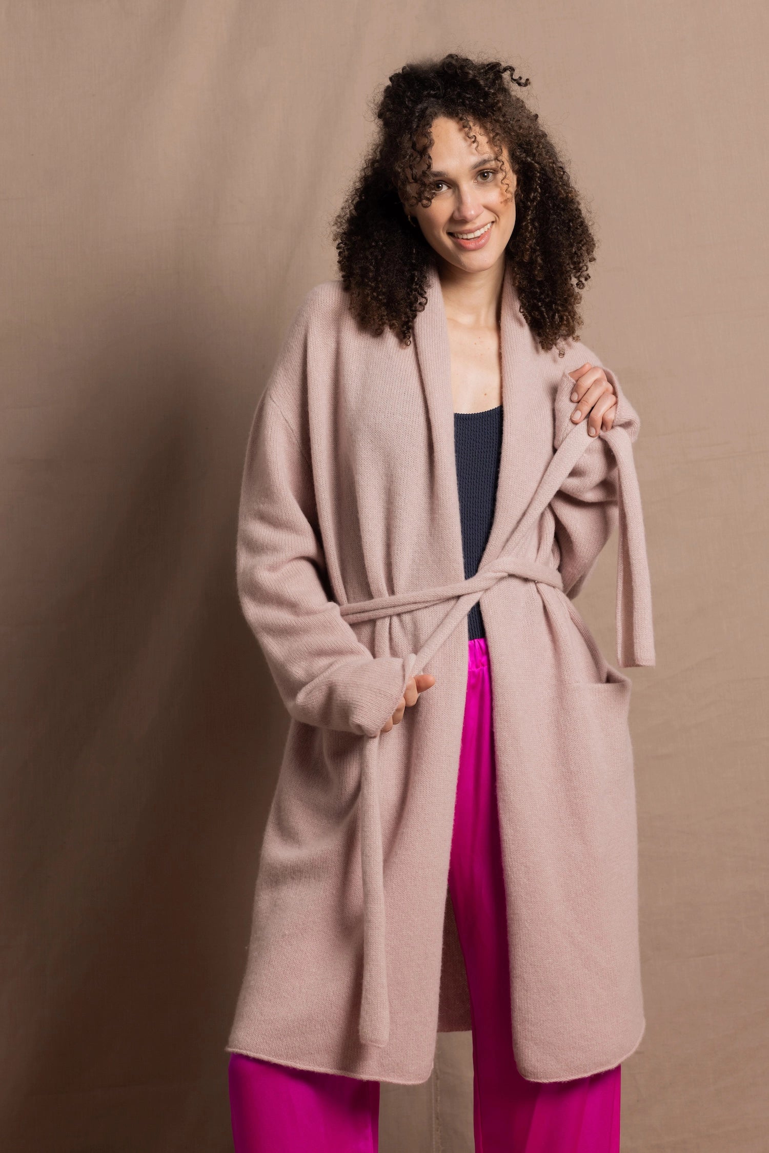 A woman wears a pure 100% cashmere dressing gown or robe in dusty pink with bright shocking pink silk trousers