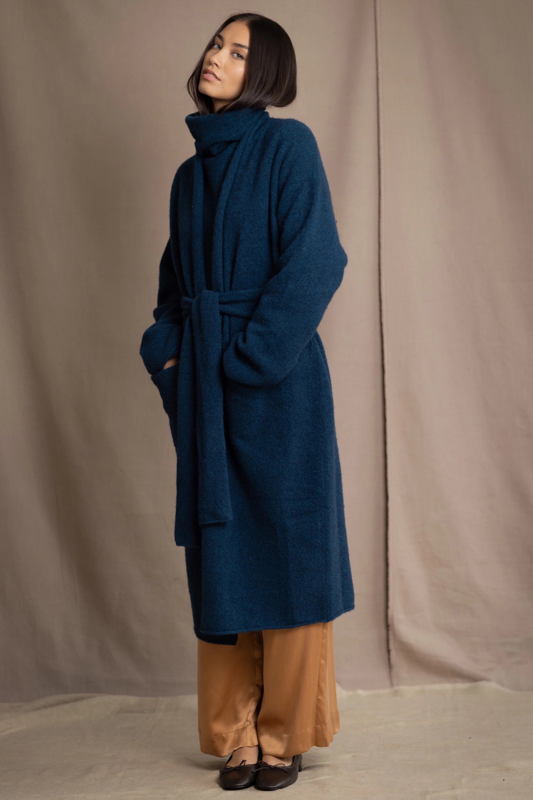 Woman wearing a long cashmere coat in teal blue over teal blue cashmere turtleneck sweater and bronze silk trousers