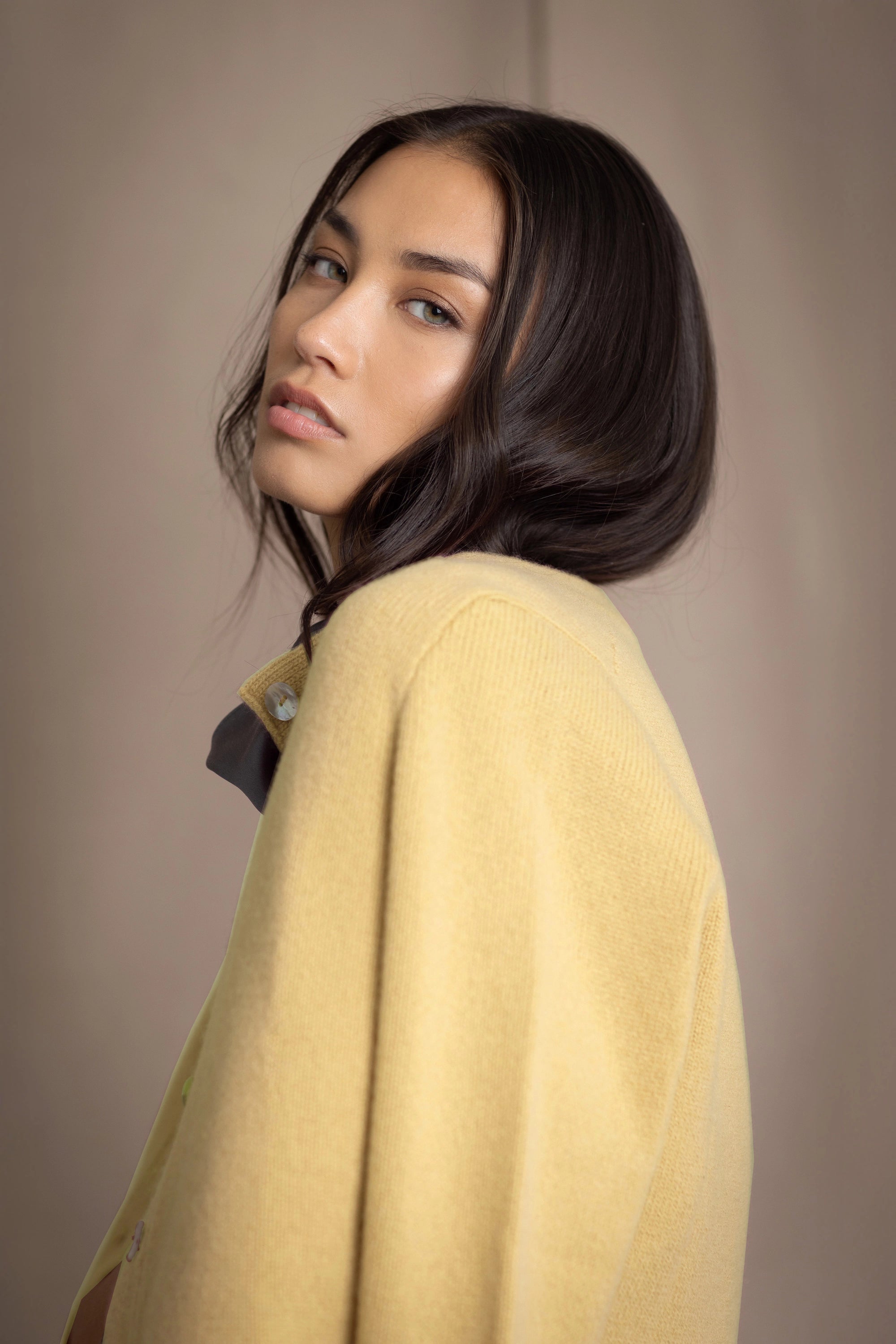 A woman wears a pale yellow cashmere cardigan over a silk top in a pewter colour
